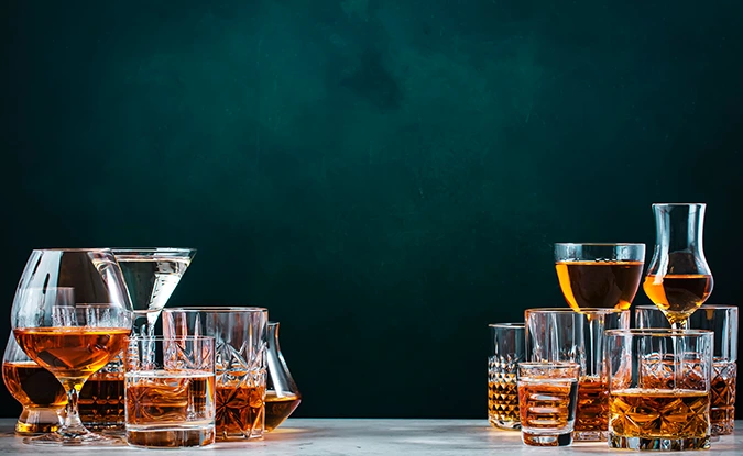 An assortment of whiskey and cognac glasses on a table against a dark green wall.