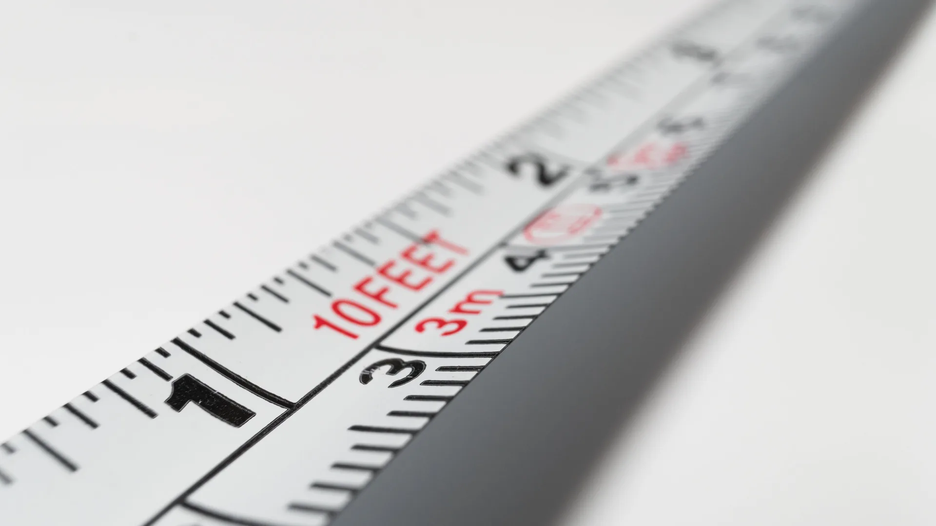 Close-up of a white tape measure printed with two scales, inches along one edge and centimeters along the other, with 10 feet and 3 m marked in red.