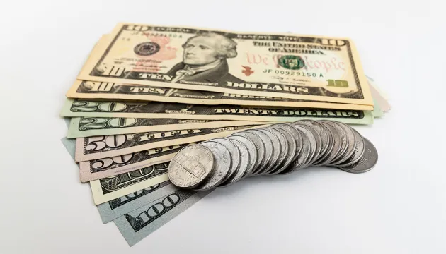 A fan of US ten, twenty, fifty and hundred dollar bills topped by a stack of quarters.