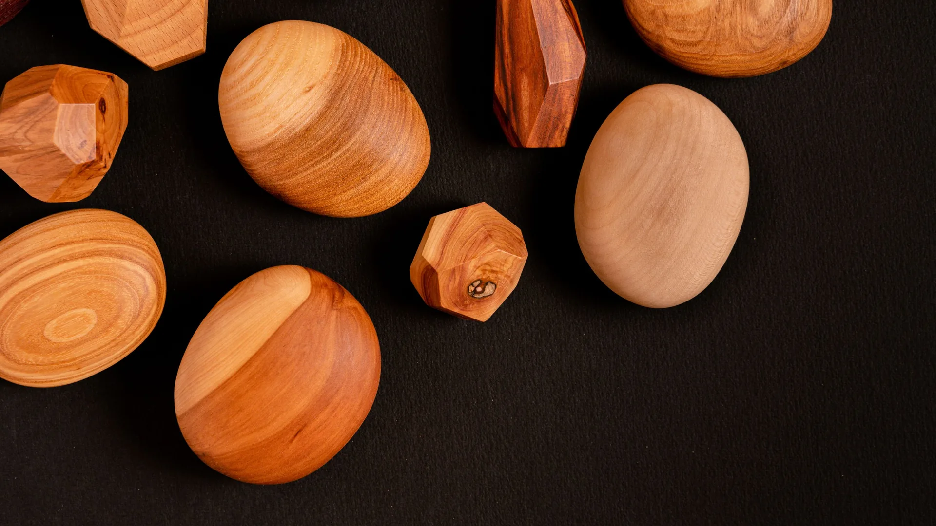 Smooth wooden pebbles and faceted wooden shapes scattered on a black surface.
