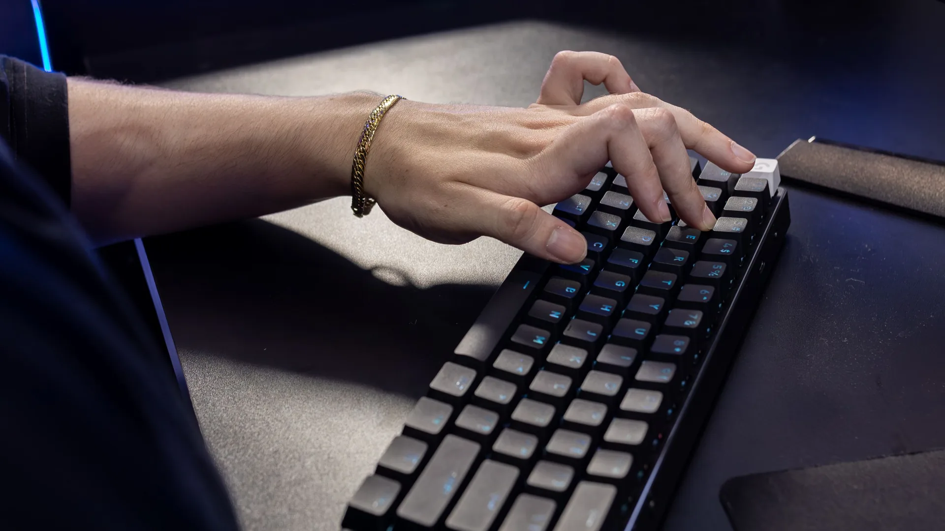 A hand types on a compact black mechanical keyboard on a dark desk.