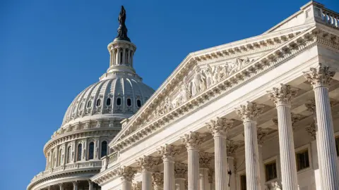 The United States Capitol dome and columned portico photographed against a clear blue sky.