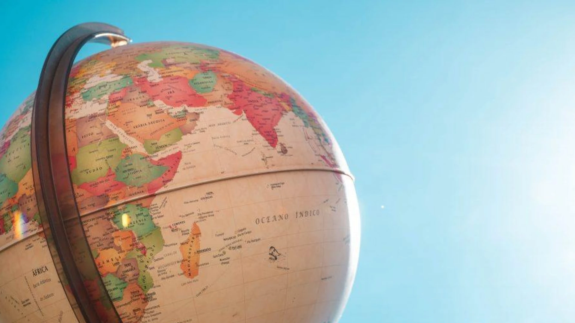A vintage style world globe in close up against a clear blue sky, showing Africa, the Arabian Peninsula and India, with place names printed in Portuguese such as Oceano Indico.
