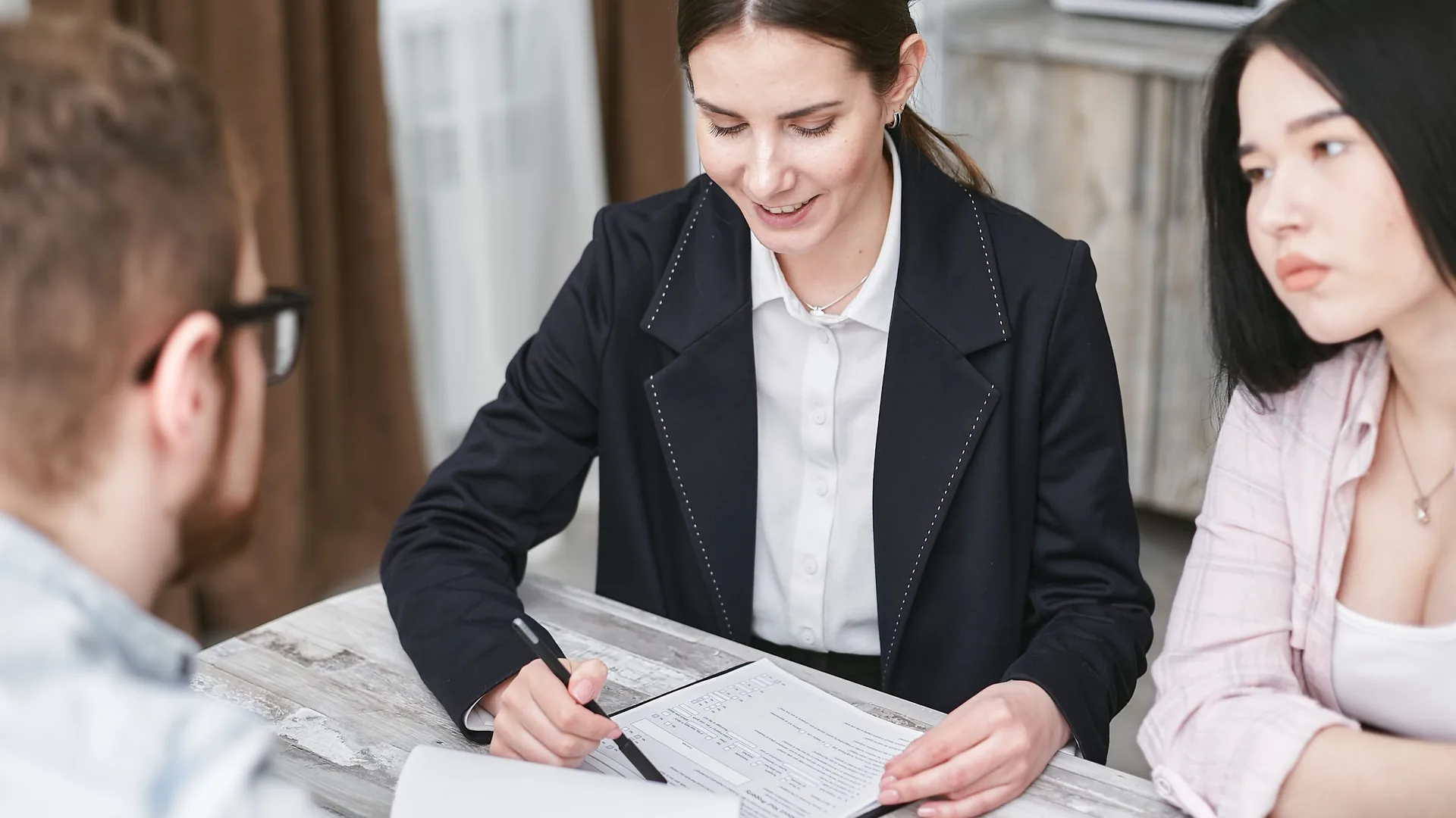 A professional in a dark blazer explains a document to two people at a table.