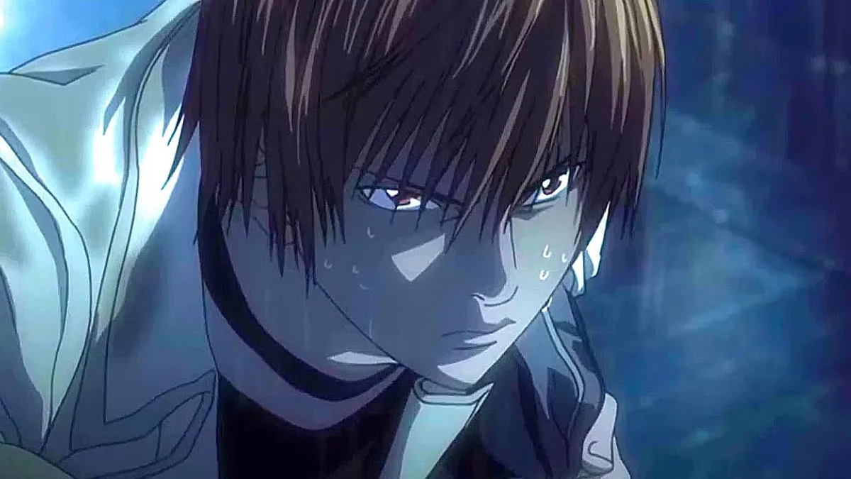 Close-up of an animated young man with swept brown hair and reddish-brown eyes, drops of sweat on his face, looking down with a tense expression against a dark blue background, with a pale jacket collar at the left.