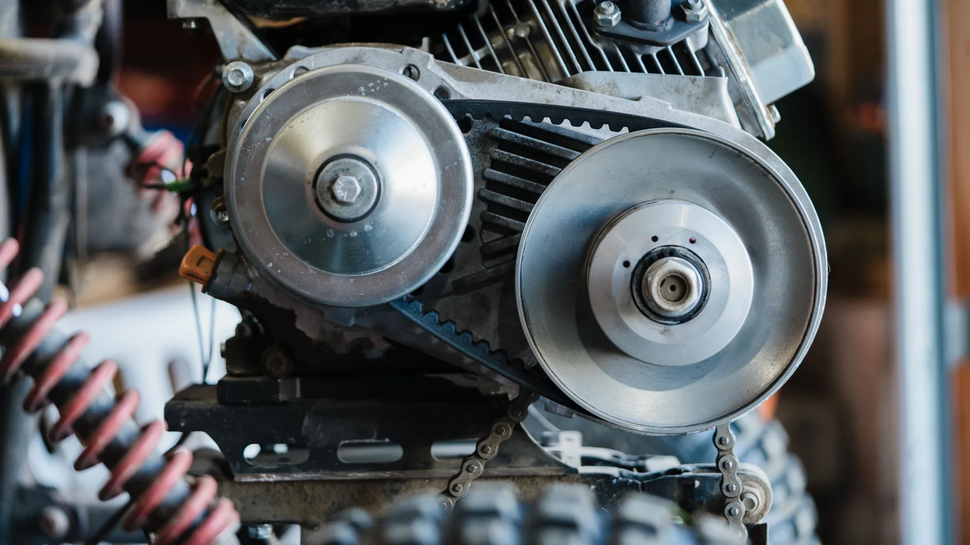 A close view of an engine with two metal pulleys joined by a toothed belt.