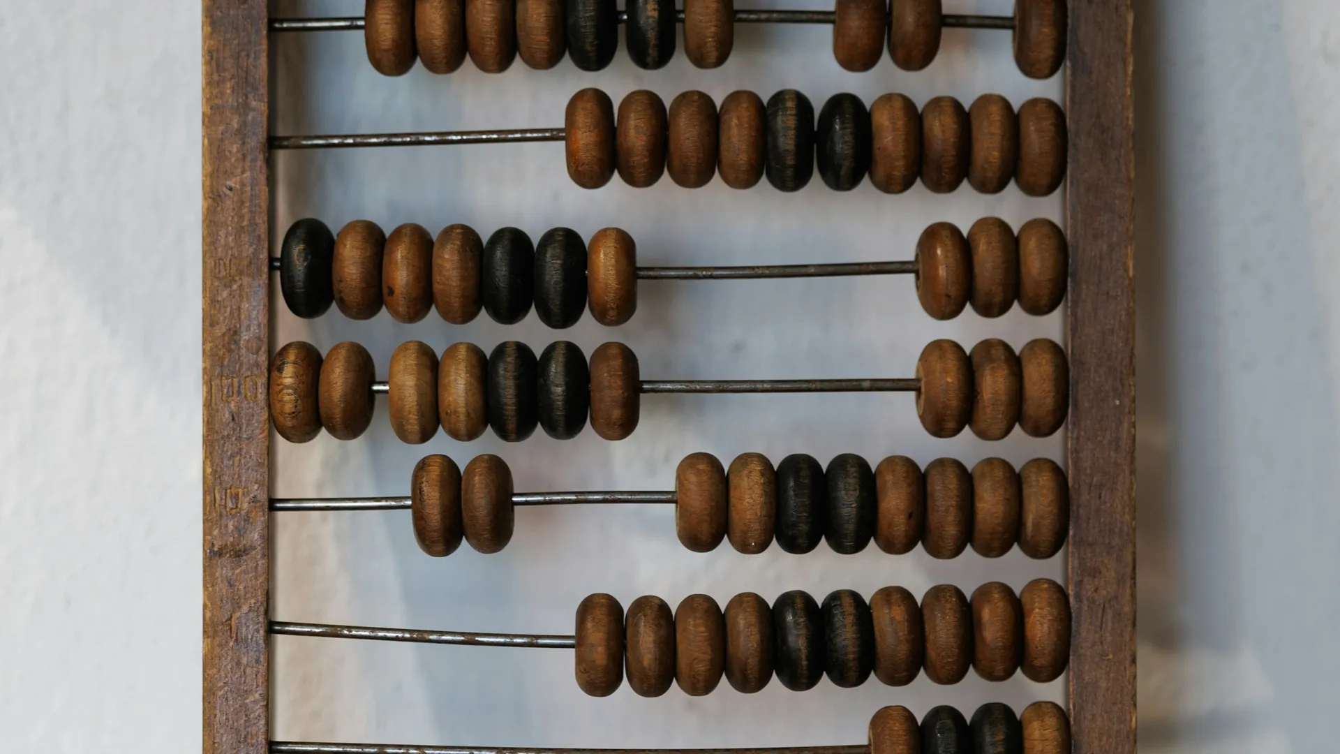 A wooden abacus with rows of dark and light beads on metal rods, standing against a white wall.