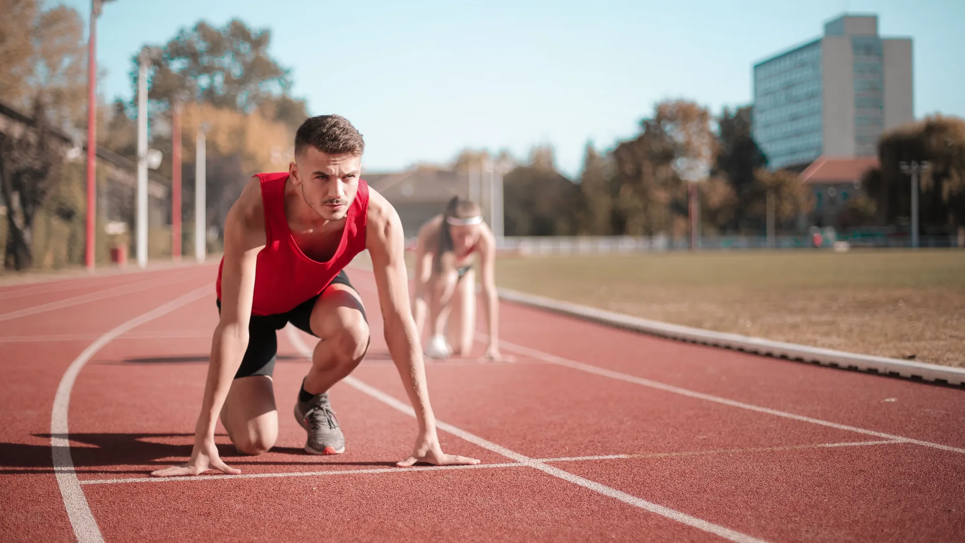 Two runners crouch in the starting position on a red running track.