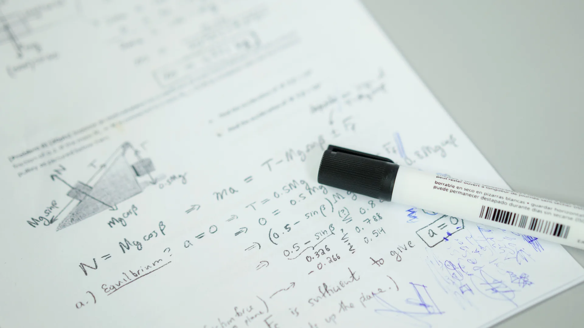 Handwritten formulas and a diagram on a sheet of paper, with a black marker lying across it.