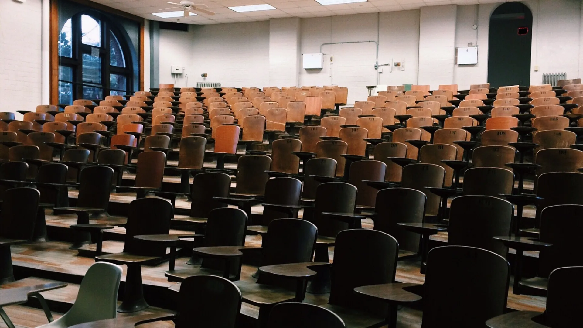 Rows of empty wooden seats with fold-down writing tablets fill a lecture hall.