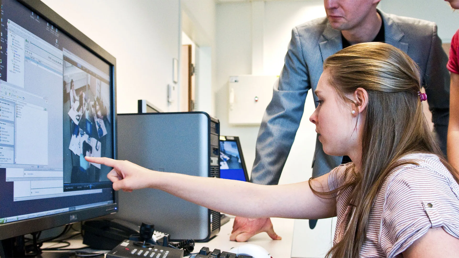 A woman points at a computer monitor in a research lab while two colleagues look on.