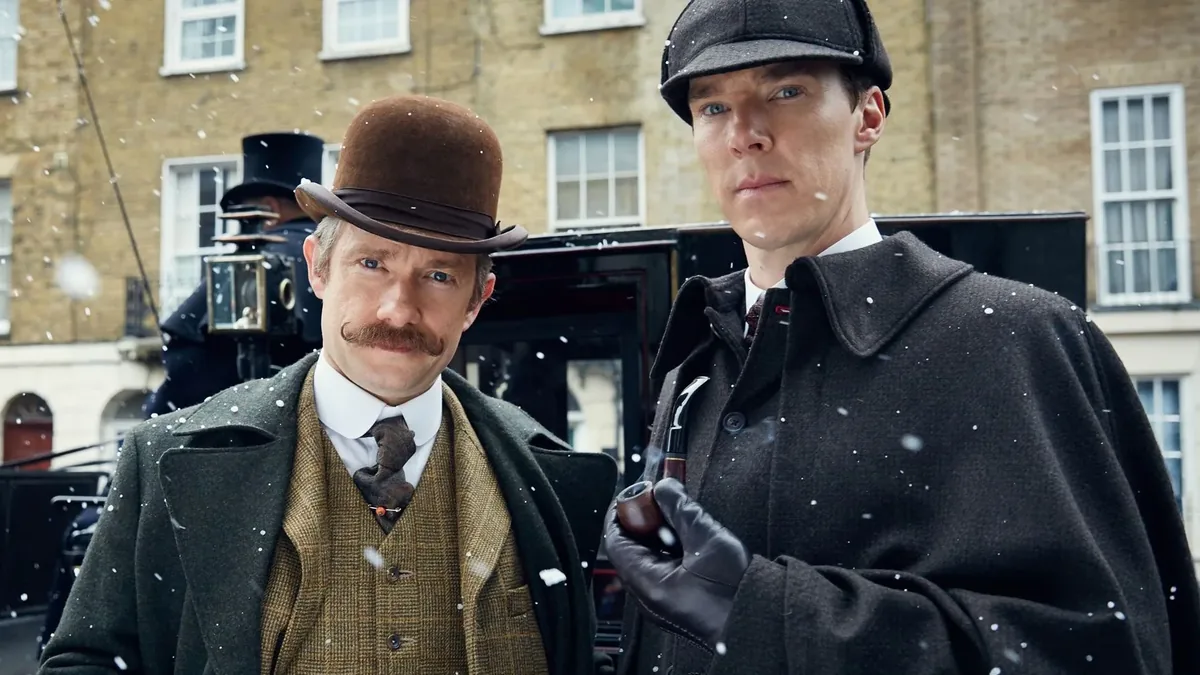 Two men in Victorian dress stand close together in falling snow in front of a horse-drawn carriage and a brick terrace, one with a brown bowler hat and a moustache, the other in a dark peaked cap with a pipe in his gloved hand.