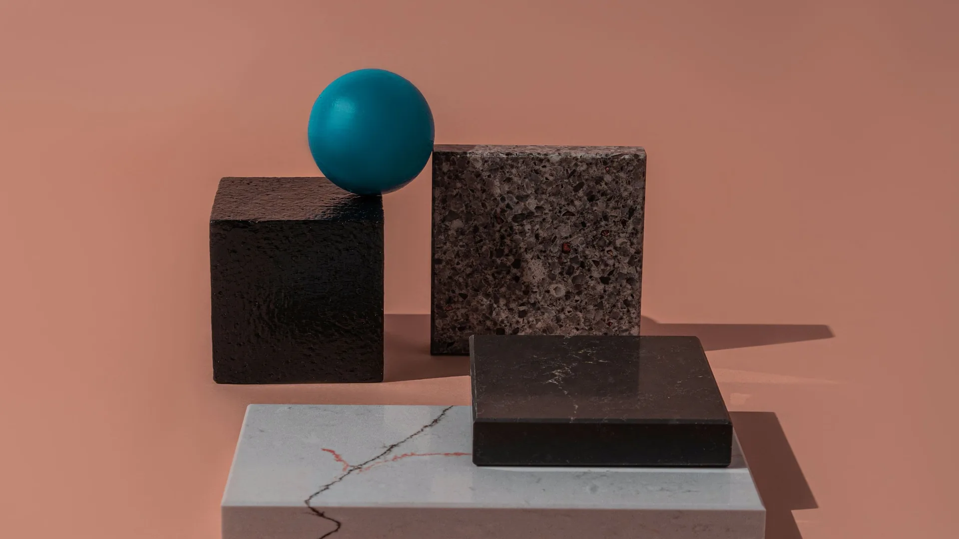 A teal sphere balanced on dark stone cubes and slabs against a pink background.