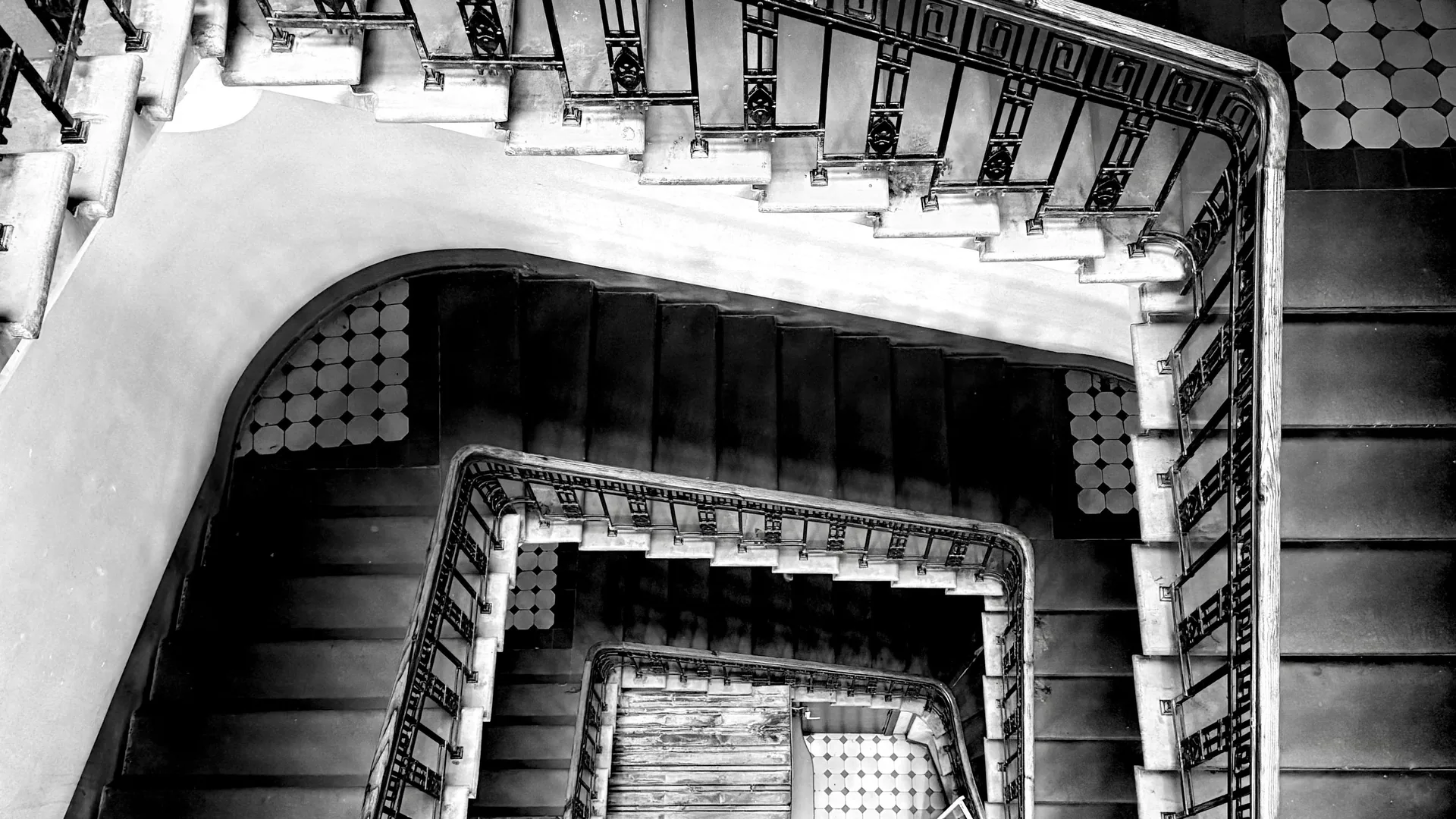 A black and white view down the square spiral of a stairwell.