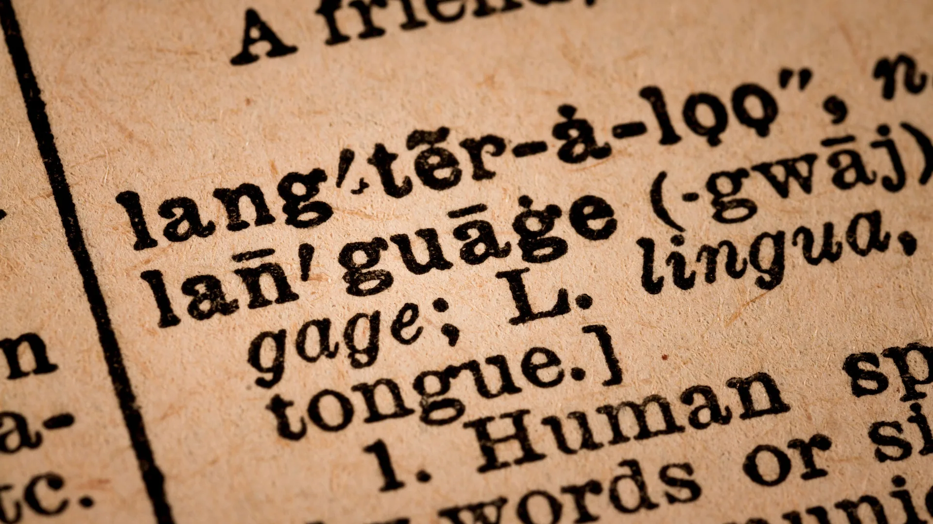 A close up of a printed dictionary page showing the entry for the word language, with its pronunciation, a bracketed note on its Latin origin and the start of the first definition, in black type on yellowed paper.